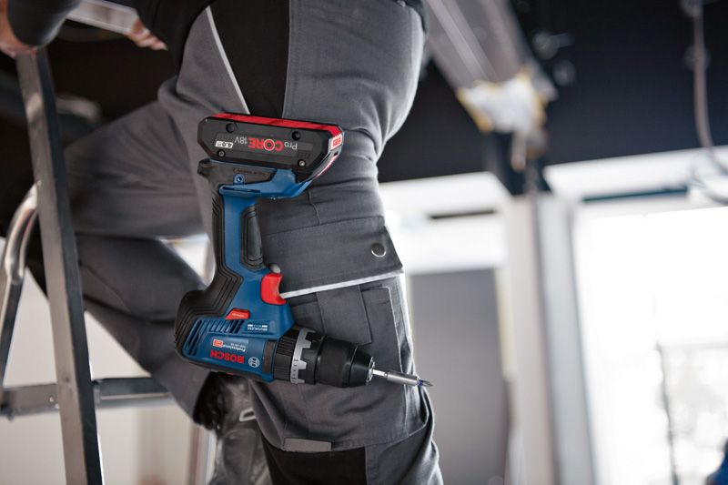 A person wearing safety equipment stands on a ladder with a cordless combi drill in their pocket.