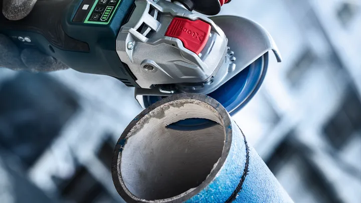 Person wearing safety equipment uses an angle grinder to cut through a metal pipe.