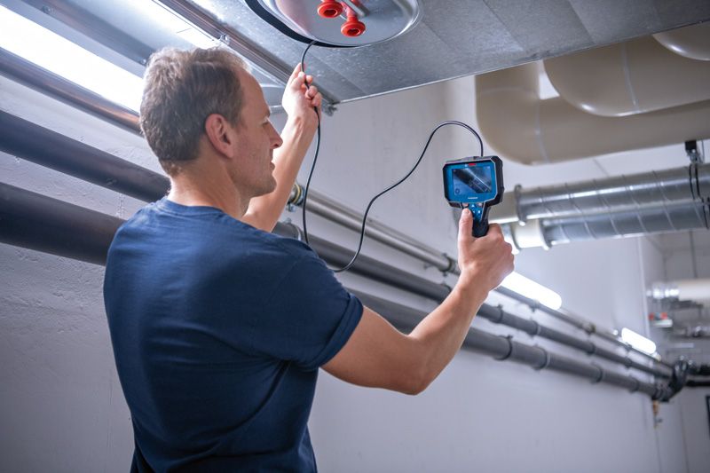 A person inspects inside an air duct using an inspection camera.