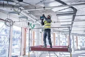 A person wearing safety equipment drills into a concrete ceiling on a construction site.