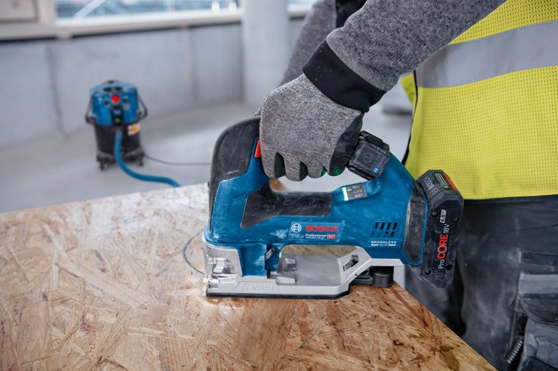 A person wearing safety equipment uses a cordless jigsaw to cut wood paneling.