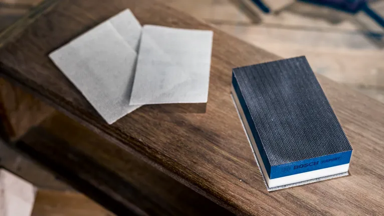 Manual sanding block and sanding sheets on a wooden surface.