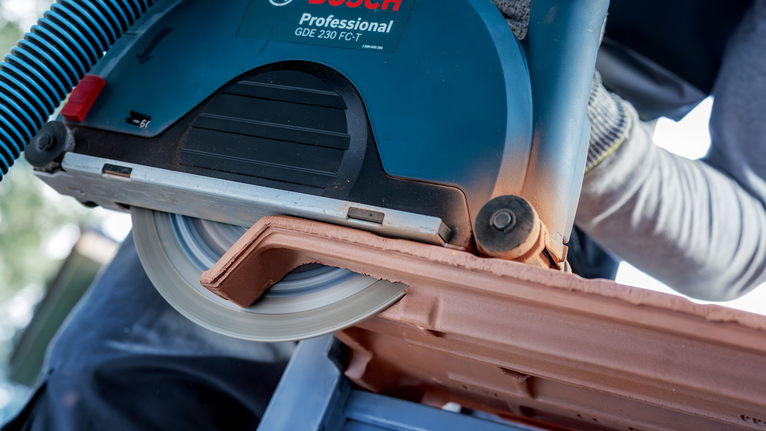 Person wearing safety equipment cuts a roof tile with a circular saw.