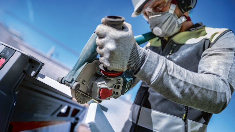 Person wearing safety equipment uses a power tool to cut metal outdoors.