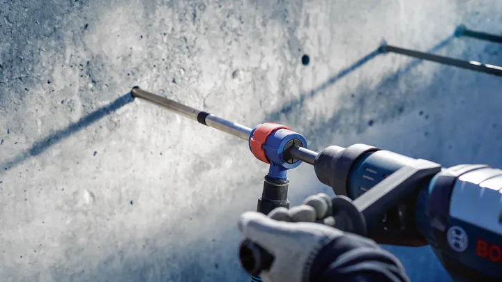 Person wearing safety equipment drills into a concrete wall.