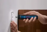 Person using a cordless screwdriver to fasten a screw into a wall switch plate.