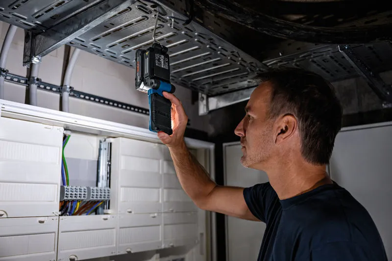 Person inspecting electrical panel using a cordless light in a utility room.
