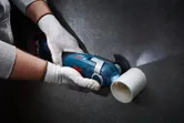 A person wearing safety equipment cuts a plastic pipe with an oscillating multi-tool.