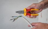 Person strips insulation from electrical wires using insulated pliers.