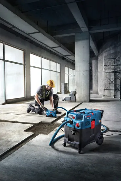 A person wearing safety equipment operates an all-purpose extractor on a concrete floor.