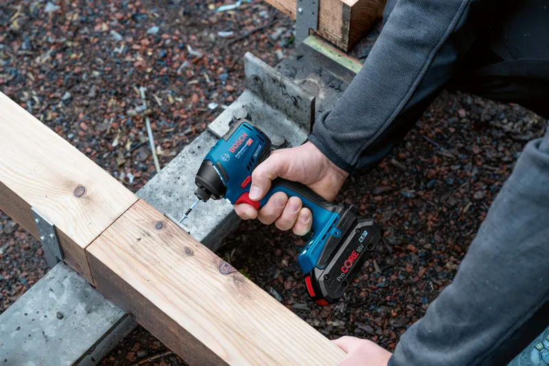 A person drives a screw into a wooden beam with a cordless impact driver.
