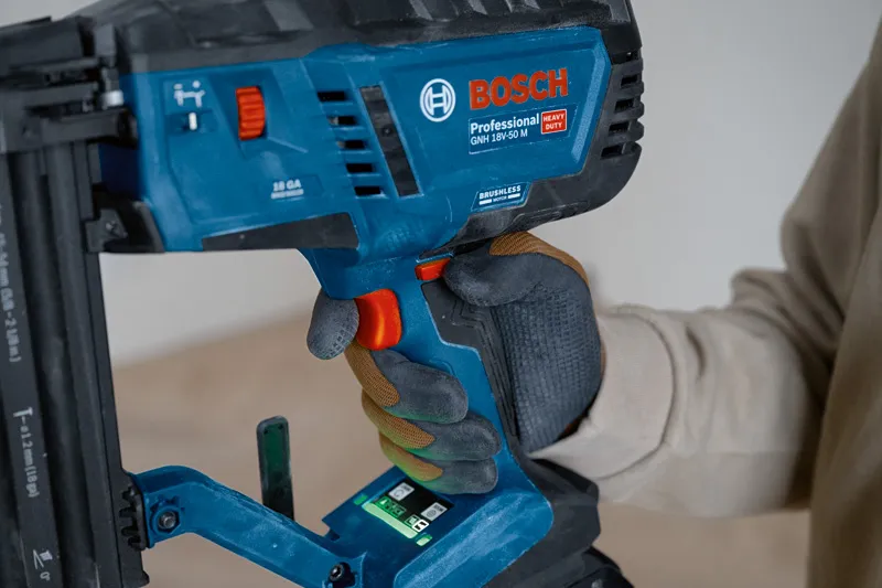A person wearing safety equipment operates a cordless wood nailer.