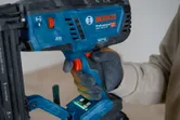 A person wearing safety equipment operates a cordless wood nailer.