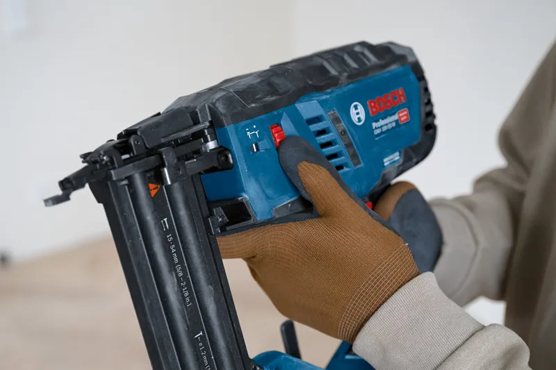 A person wearing safety equipment adjusts a cordless wood nailer.