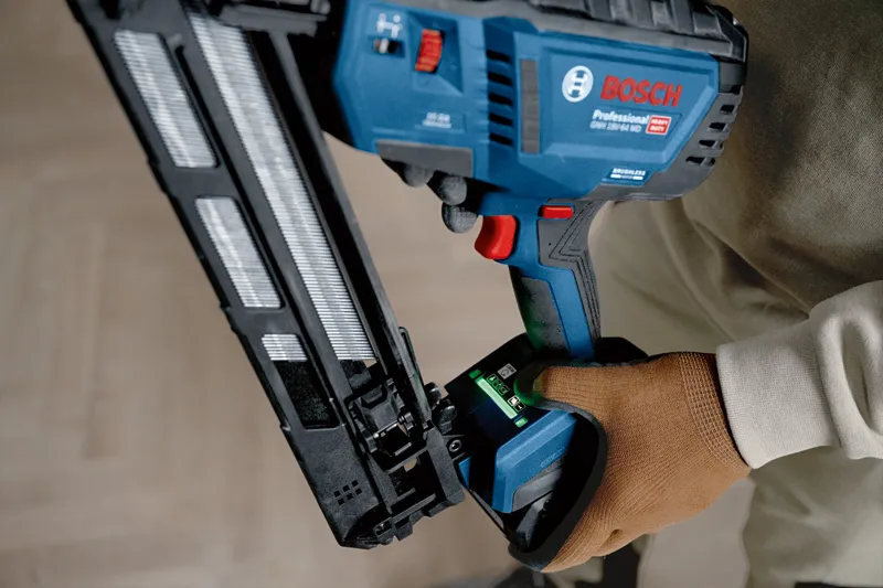 Person wearing safety equipment operates a cordless wood nailer indoors.