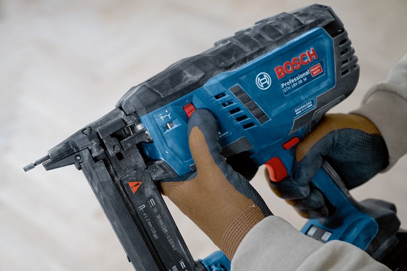 Person wearing safety equipment adjusts a cordless wood stapler.