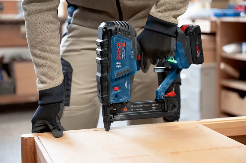 A person wearing safety equipment uses a cordless wood stapler on a wooden surface.