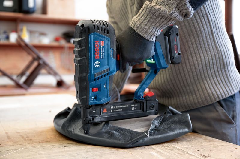 Person wearing safety equipment uses a cordless wood stapler to fasten upholstery.