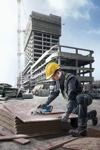 A person wearing safety equipment cuts stacked plywood at a construction site.
