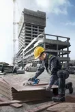 A person wearing safety equipment cuts stacked plywood at a construction site.