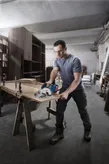 A person wearing safety equipment uses a circular saw to cut plywood in a workshop.