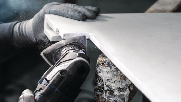 Person wearing safety equipment cuts a corner from a white countertop with a power tool.