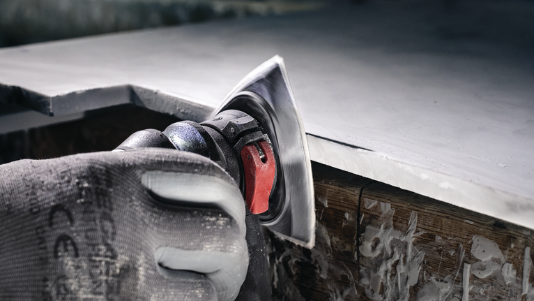 Person wearing safety equipment polishes the edge of a countertop with a power tool.