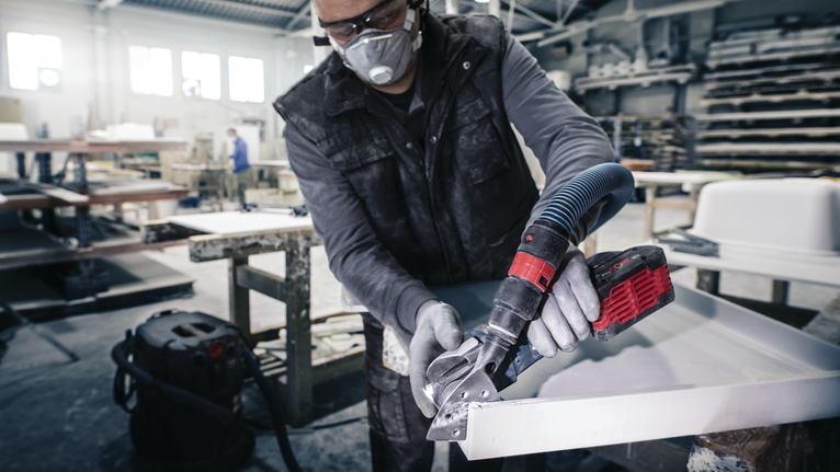 Person wearing safety equipment polishes the edge of a countertop with a power tool.