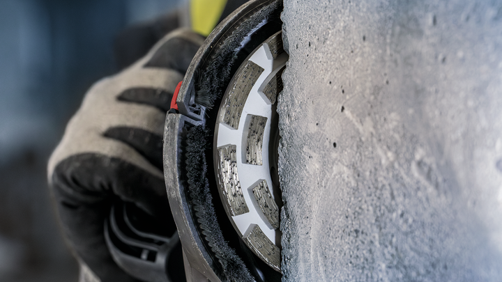 A person wearing safety equipment grinds concrete with a diamond wheel.