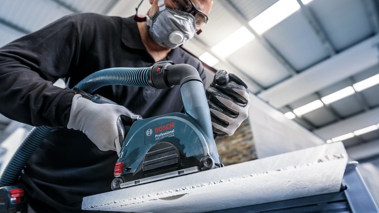Person wearing safety equipment sands a concrete surface with a power tool.