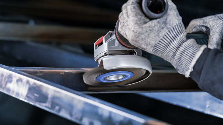 Person wearing safety equipment grinding a metal beam with an angle grinder.