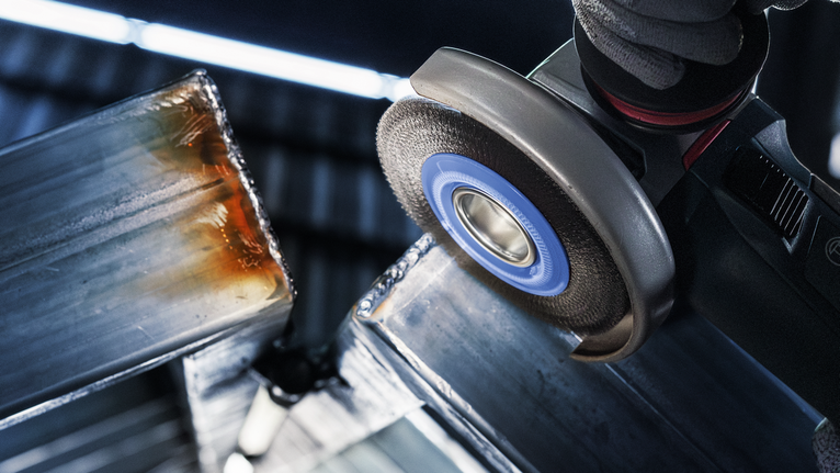 Person wearing safety equipment grinds metal beams using an angle grinder.