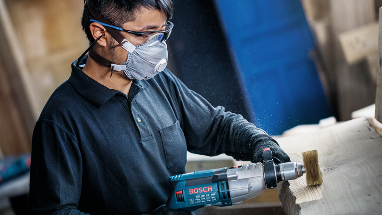 Person wearing safety equipment sands a wooden beam with a power tool.