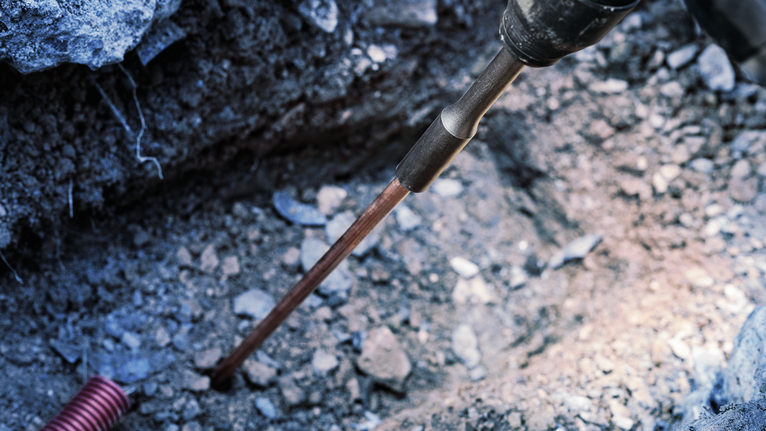 Power tool drilling into rocky ground at a construction site.
