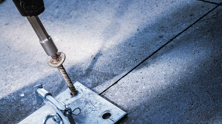 Person wearing safety equipment chiseling rebar set in concrete.