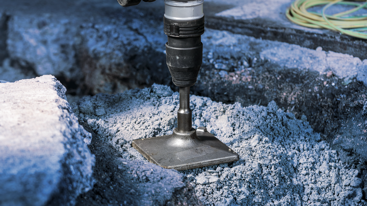 A power tool breaks through concrete with a flat chisel attachment.