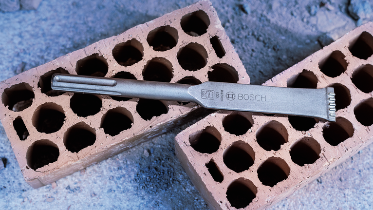 Chisel bit placed on two perforated bricks at a construction site.