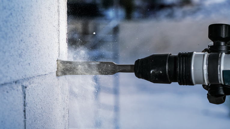 Rotary hammer chisel breaking concrete block wall.