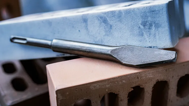 Chisel bit resting on stacked concrete and clay bricks.