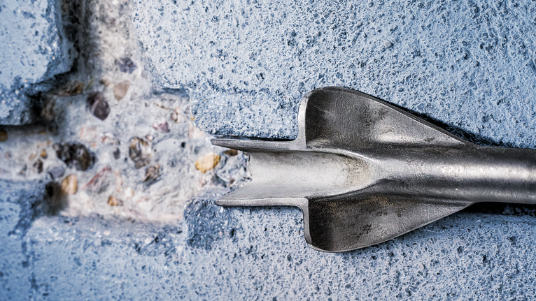 Chisel bit breaking through a concrete wall.