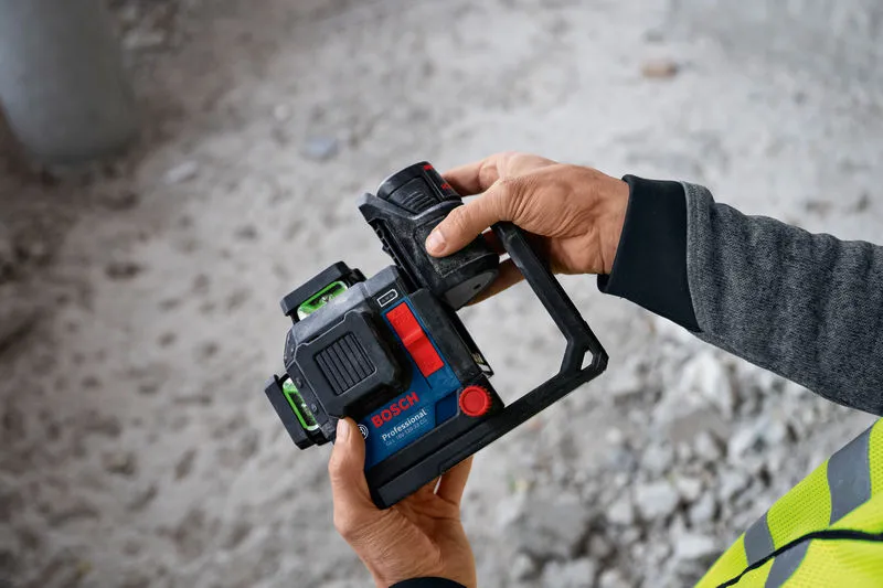Person wearing safety equipment holding a laser leveling tool with attached battery.