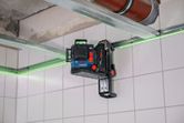Laser leveling tool mounted on a wall track accessory projects green lines across tiled walls.