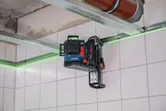 Laser leveling tool mounted on a wall track accessory projects green lines across tiled walls.