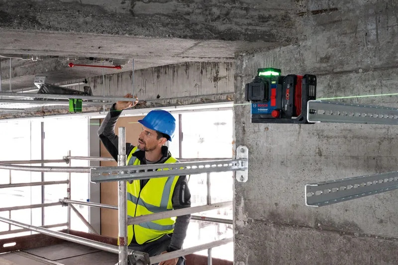 A person wearing safety equipment aligns metal bars using a laser leveling tool.