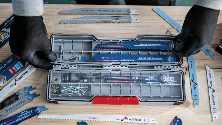 Person wearing safety equipment organizing saw blades and screws in a tool case.