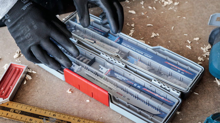 Person wearing safety equipment selects blades from a tool case on a workbench.