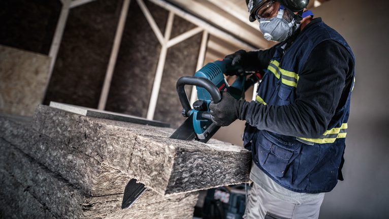 Person wearing safety equipment cuts insulation panels with a reciprocating saw.