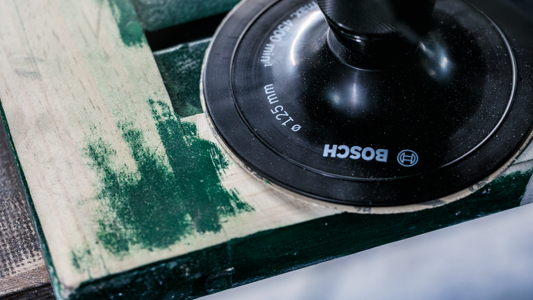 Sander removing green paint from a wooden surface.