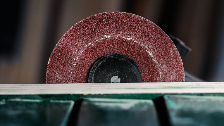 Cutting wheel slices through a wooden board in a workshop setting.