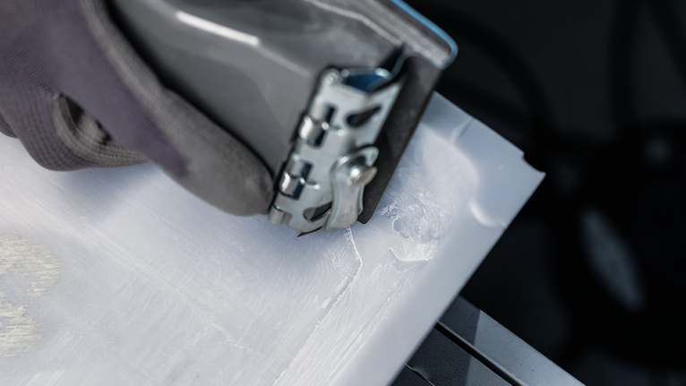 Person wearing safety equipment operates a power tool to cut a plastic sheet.